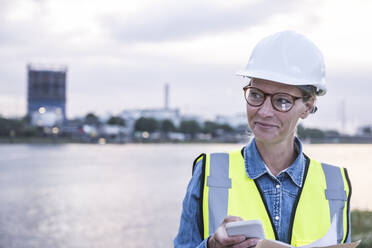 Lächelnde Arbeiterin, die ihr Smartphone in der Hand hält - UUF23776