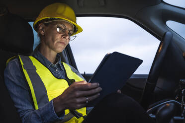 Reife weibliche Berufstätige, die im Auto sitzend ein digitales Tablet benutzt - UUF23782