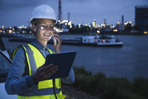 Eine Logistikmitarbeiterin spricht mit einem Smartphone und hält ein digitales Tablet in der Hand - UUF23794