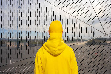 Boy wearing yellow sweatshirt in front of metallic wall on sunny day - VPIF04221