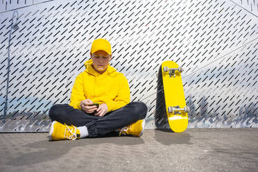 Einsamer männlicher Skater mit Smartphone am gelben Skateboard - VPIF04229
