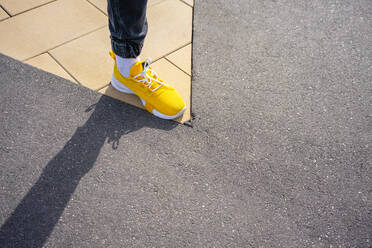 Boy wearing yellow shoe while standing on footpath - VPIF04233