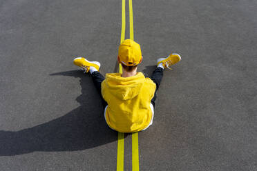 Boy sitting over yellow road marking on sunny day - VPIF04241