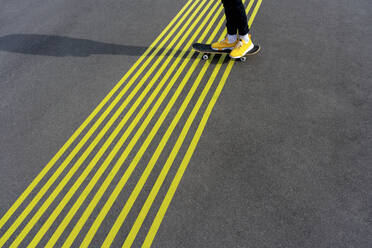 Junge mit Skateboard über gelbe Straßenmarkierungen an einem sonnigen Tag - VPIF04245