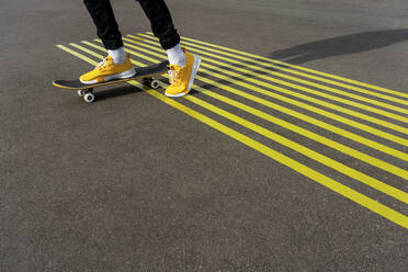 Boy riding skateboard on road with parallel yellow markings - VPIF04246