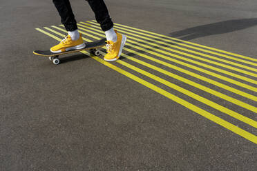 Junge fährt Skateboard auf einer Straße mit parallelen gelben Markierungen - VPIF04246