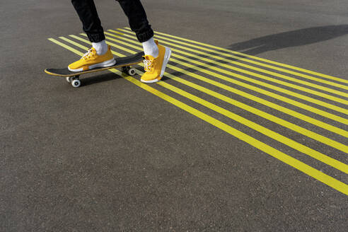 Boy riding skateboard on road with parallel yellow markings - VPIF04246