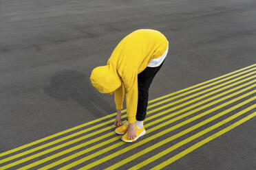 Boy touching toes while bending over yellow markings on road - VPIF04254