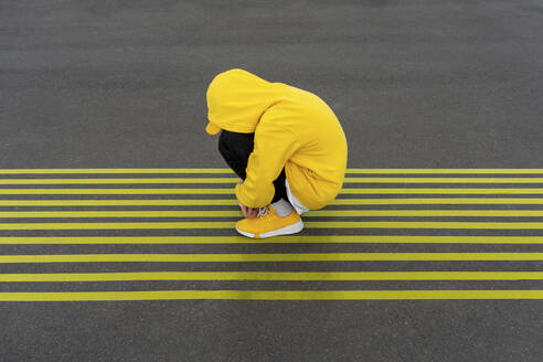 Depressed boy crouching on striped yellow road markings - VPIF04255