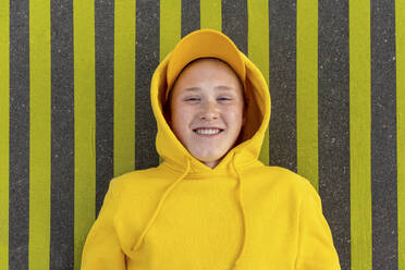 Smiling boy in yellow sweatshirt lying on road marking - VPIF04257