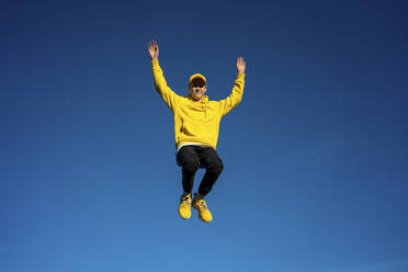 Carefree boy with arms raised jumping on sunny day - VPIF04278