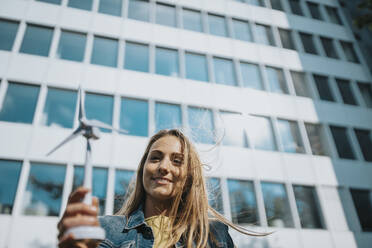 Frau hält Modell einer Windkraftanlage vor einem modernen Bürogebäude - MFF08226