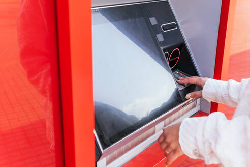 Abgeschnittene, nicht erkennbare Frau, die einen Geldautomaten benutzt und Geld abhebt, während sie auf der Straße steht - ADSF25248