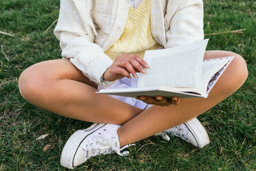 Abgeschnittene unerkennbare Frau sitzt im Park und liest ein interessantes Buch im Sommer - ADSF25258