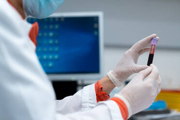 Unbekannte Ärztin mit Maske und Handschuhen hält ein Röhrchen mit einer Blutprobe in einem modernen Labor in einer Klinik - ADSF25272