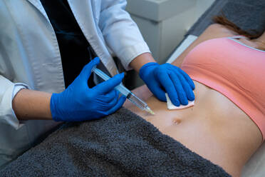 Von oben der Ernte anonyme professionelle Kosmetikerin macht Injektion für Frau während Cellulite-Behandlung in Schönheitsklinik - ADSF25291