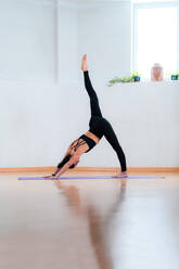 Side view of female in sportswear showing Three Legged Downward Facing Dog pose in room - ADSF25301