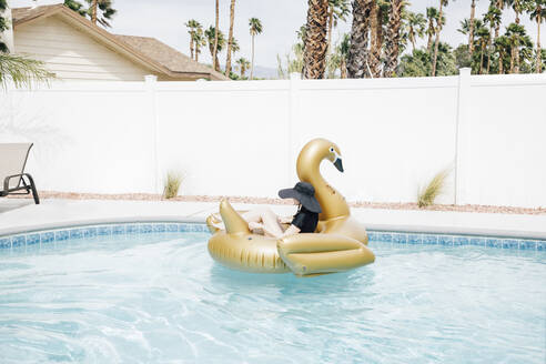 Woman relaxing on inflatable swan in swimming pool - ACTF00102