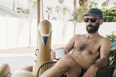 Shirtless man having coffee while relaxing at patio - ACTF00108