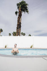 Mid adult man looking away while standing in swimming pool during sunny day - ACTF00110