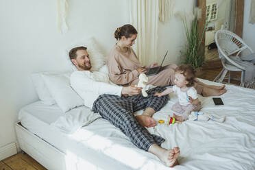 Mann spielt mit Tochter von Frau mit Laptop auf Bett zu Hause - VPIF04292