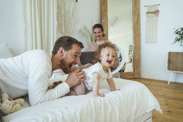 Smiling woman looking at cheerful man playing with daughter in bedroom - VPIF04298