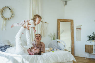 Happy woman looking at cheerful daughter picked up by man on bed at home - VPIF04301