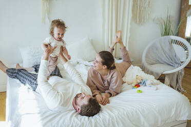 Smiling woman looking at daughter lifted by father at bedroom - VPIF04302