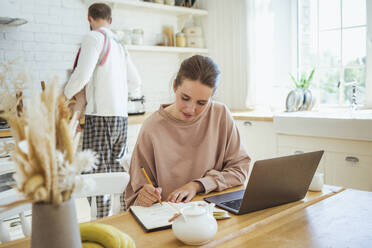 Businesswoman writing on diary with man and daughter in kitchen at home - VPIF04303