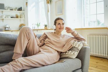 Young woman looking away while listening music through headphones on sofa at home - VPIF04311