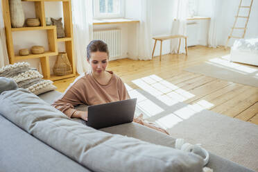 Young businesswoman using laptop while sitting on floor at home - VPIF04313