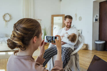 Frau fotografiert Mann, der seine Tochter zu Hause auf einem Stuhl trägt - VPIF04315