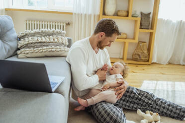 Man looking at daughter sleeping on lap in living room - VPIF04317