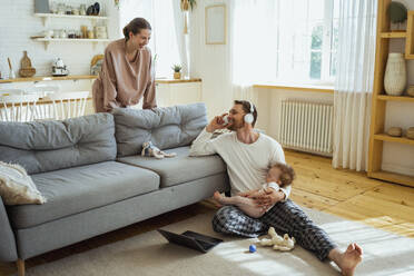 Smiling woman looking at businessman talking on mobile phone at home - VPIF04323