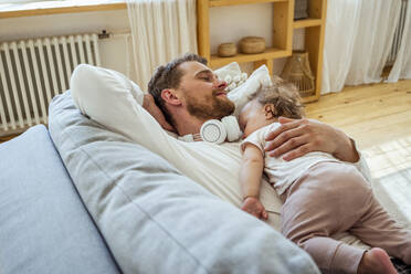 Man with daughter sleeping on sofa at home - VPIF04326
