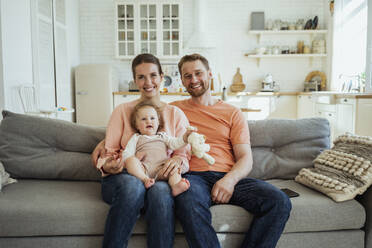 Lächelnder Mann und lächelnde Frau auf dem Sofa mit Tochter auf dem Schoß zu Hause - VPIF04338