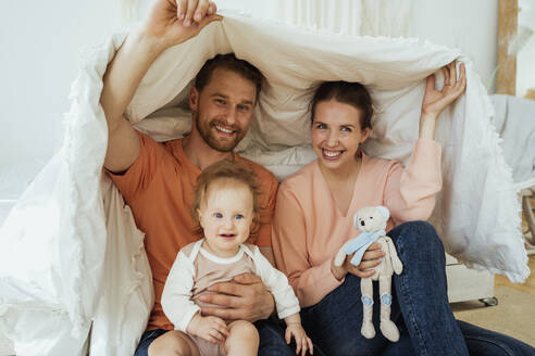 Lächelnder Mann und lächelnde Frau mit einer in eine Decke gehüllten Tochter zu Hause - VPIF04342