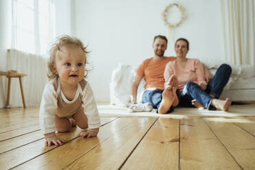 Nettes Mädchen krabbelt, während Mutter und Vater zu Hause auf dem Boden sitzen - VPIF04344
