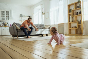 Father calling daughter crawling on floor at home - VPIF04353