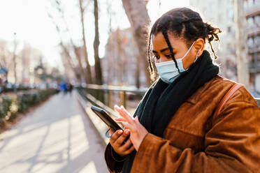 Italien, Frau mit Gesichtsmaske schreibt im Freien eine SMS - ISF24696