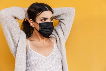 Portrait of Spanish brunette girl with face mask holding her hair on yellow background wall. - CAVF94397