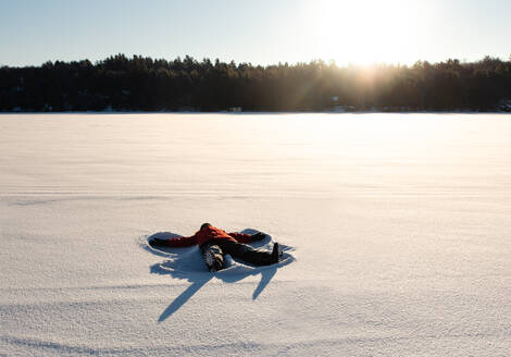 Ein Kind macht einen Schneeengel auf einer verschneiten Wiese in der Morgensonne. - CAVF94420