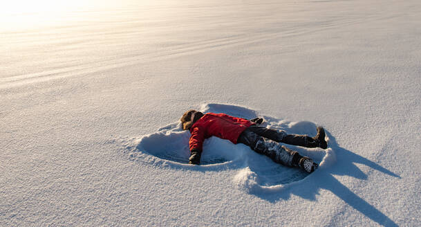 Ein Kind macht einen Schneeengel auf einer verschneiten Wiese in der Morgensonne. - CAVF94422