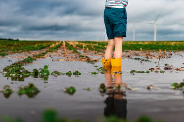 Ein Kind steht im überschwemmten Wasser auf einem Sojabohnenfeld in der Nähe eines Windparks - CAVF94434
