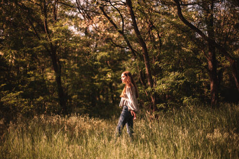 Teenager-Mädchen geht durch grünes Gras im Wald im Sommer - CAVF94520