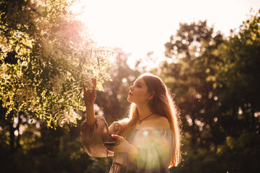 Teenage girl touching flowering branch in park during summer - CAVF94522