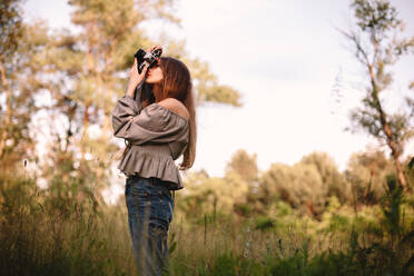 Junge Frau fotografiert mit Kamera im Sommerwald stehend - CAVF94524