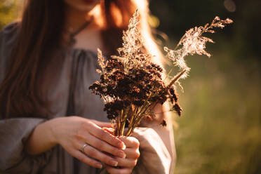 Close up of young woman holding bouquet of dried flowers in summer - CAVF94525