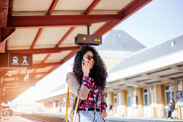 Glückliches junges afrikanisches Mädchen, das am Bahnhof in Europa mit einem Handy telefoniert - CAVF94561