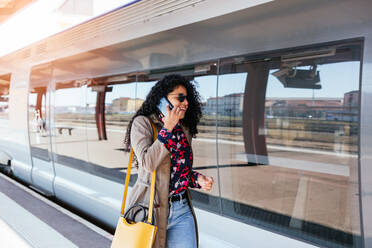 Happy young African girl talking on cell phone at train station in Europe - CAVF94562